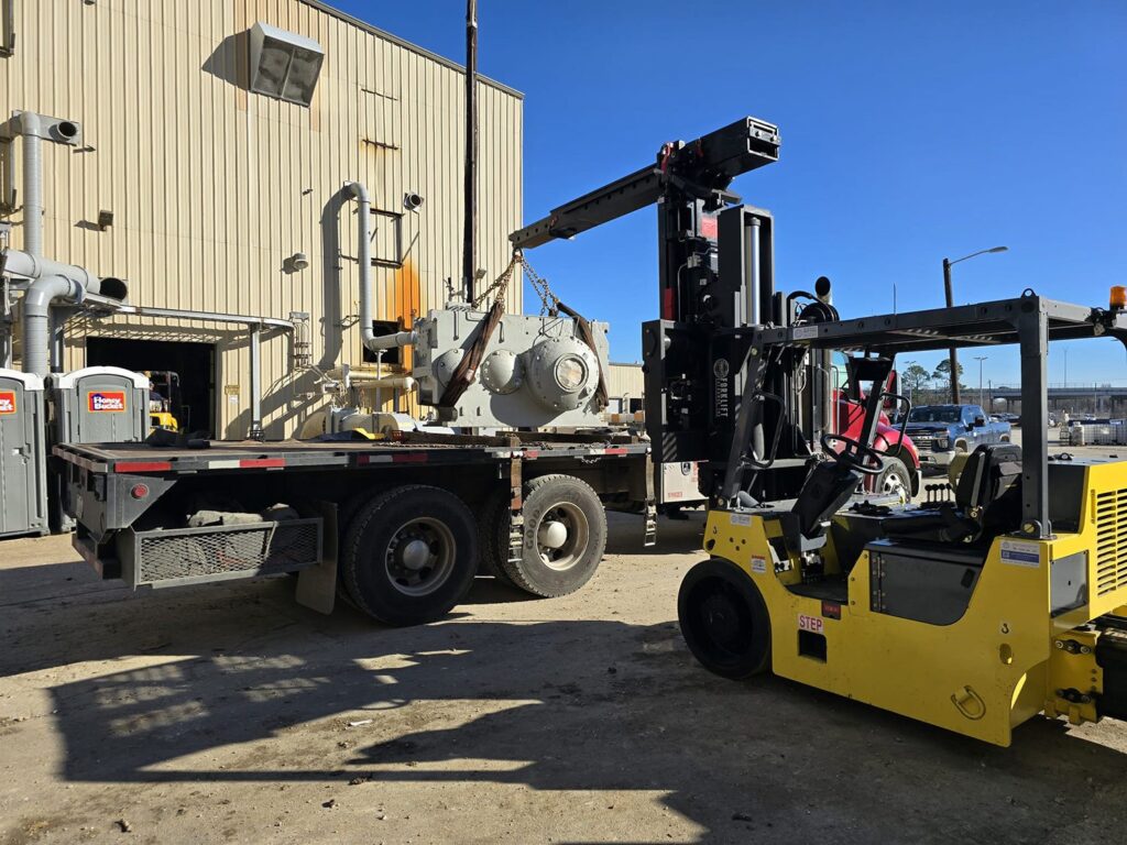 Forklift crane lifting heavy machinery onto a flatbed trailer